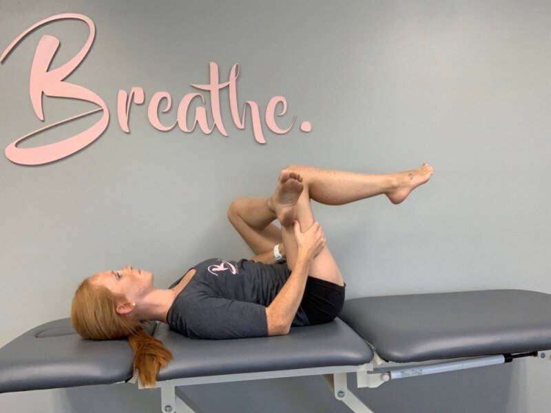 woman laying on a table with one leg crossed over the other stretching her glute muscle.